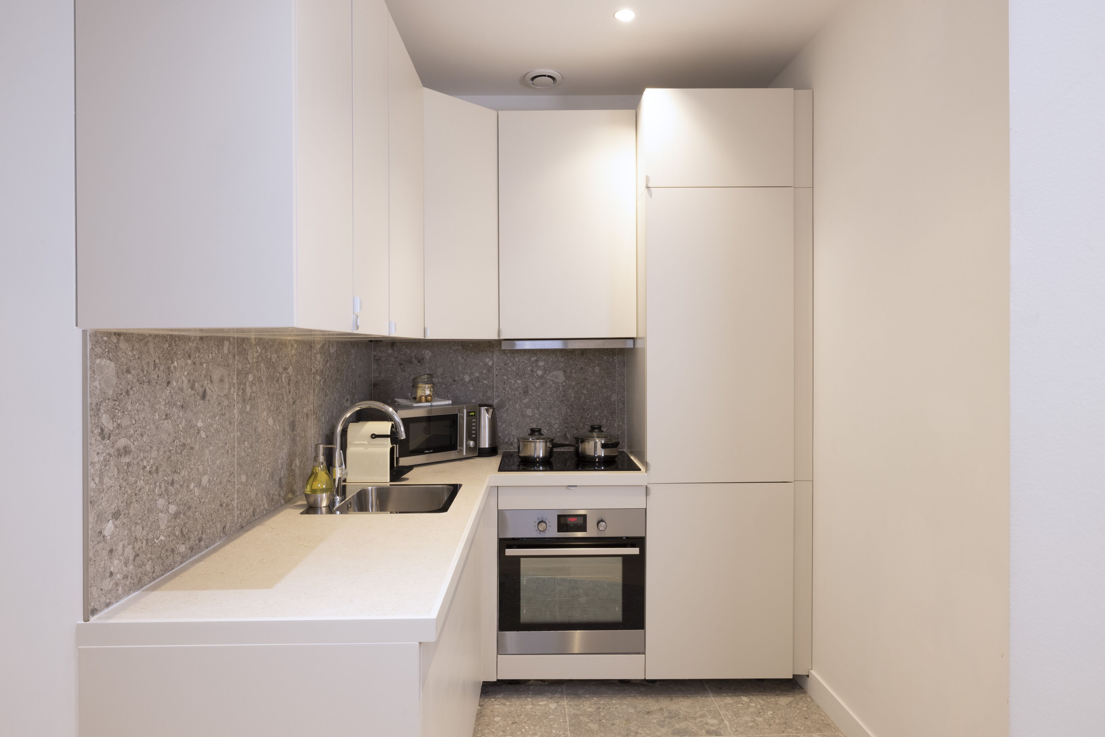 A compact kitchen with white cabinets, a granite countertop, a stainless steel sink, a microwave, a stove, and an oven.