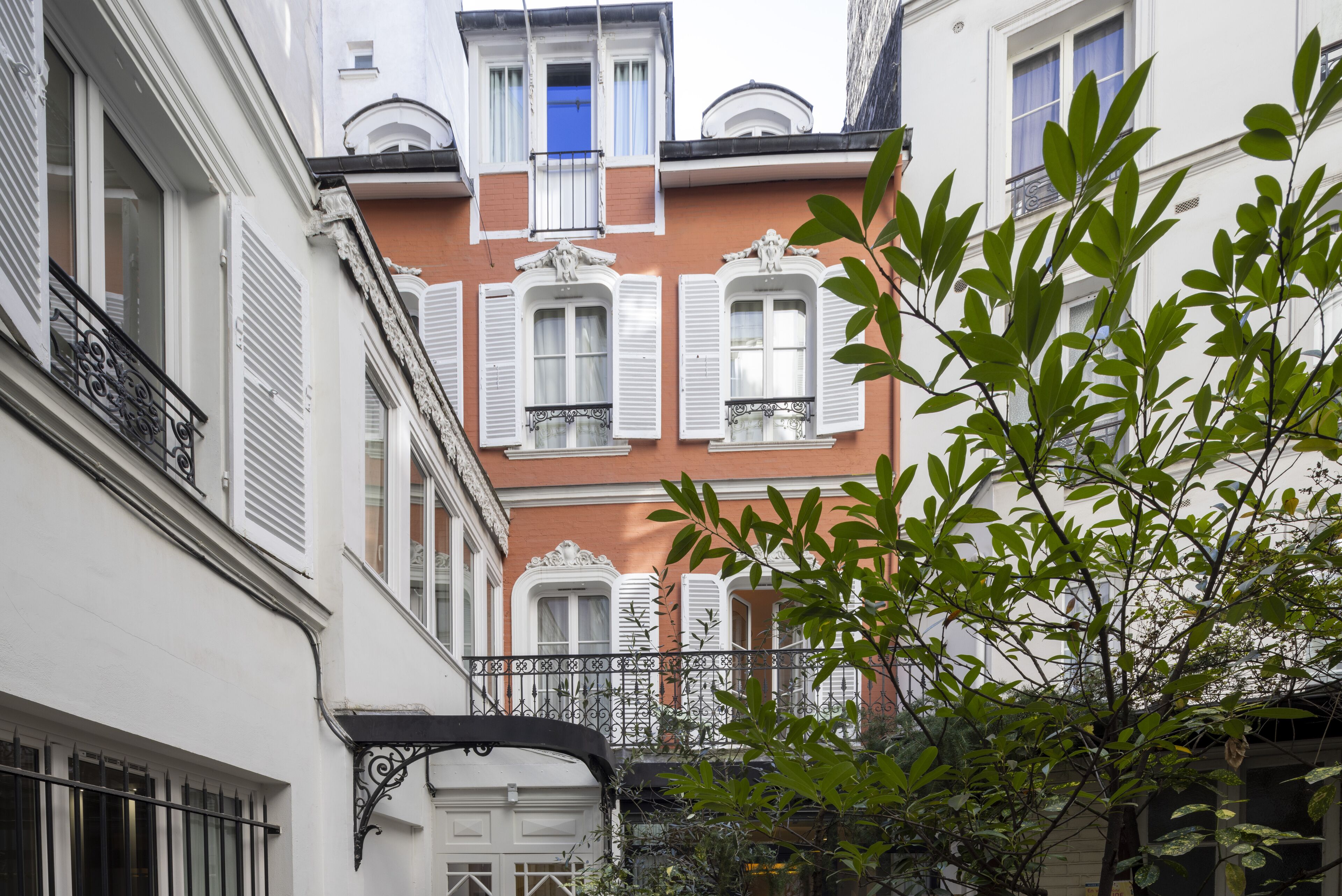 A narrow street with buildings featuring white and red facades, shutters, and balconies.