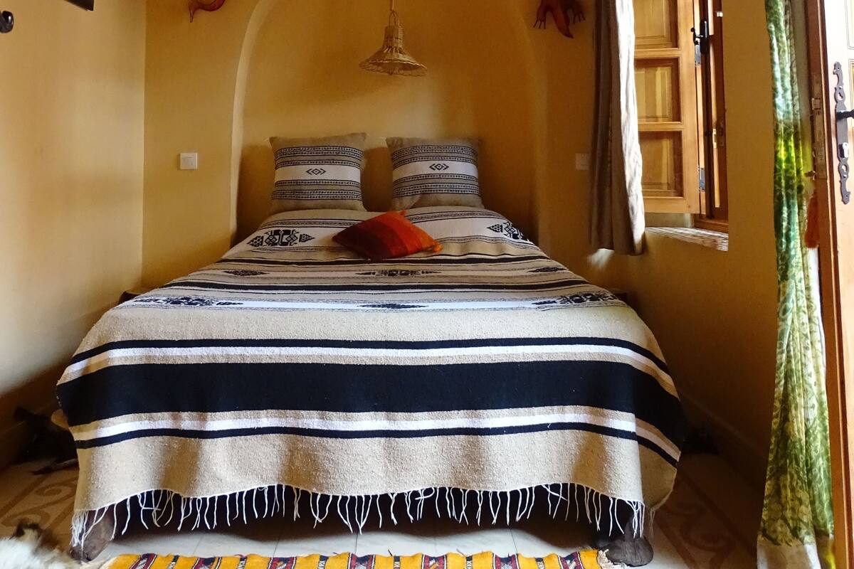A bed with a striped blanket and pillows, a hanging light fixture, and a framed picture on the wall.