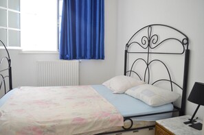 Una cama con colcha estampada, cortina azul y cabecero de metal negro.