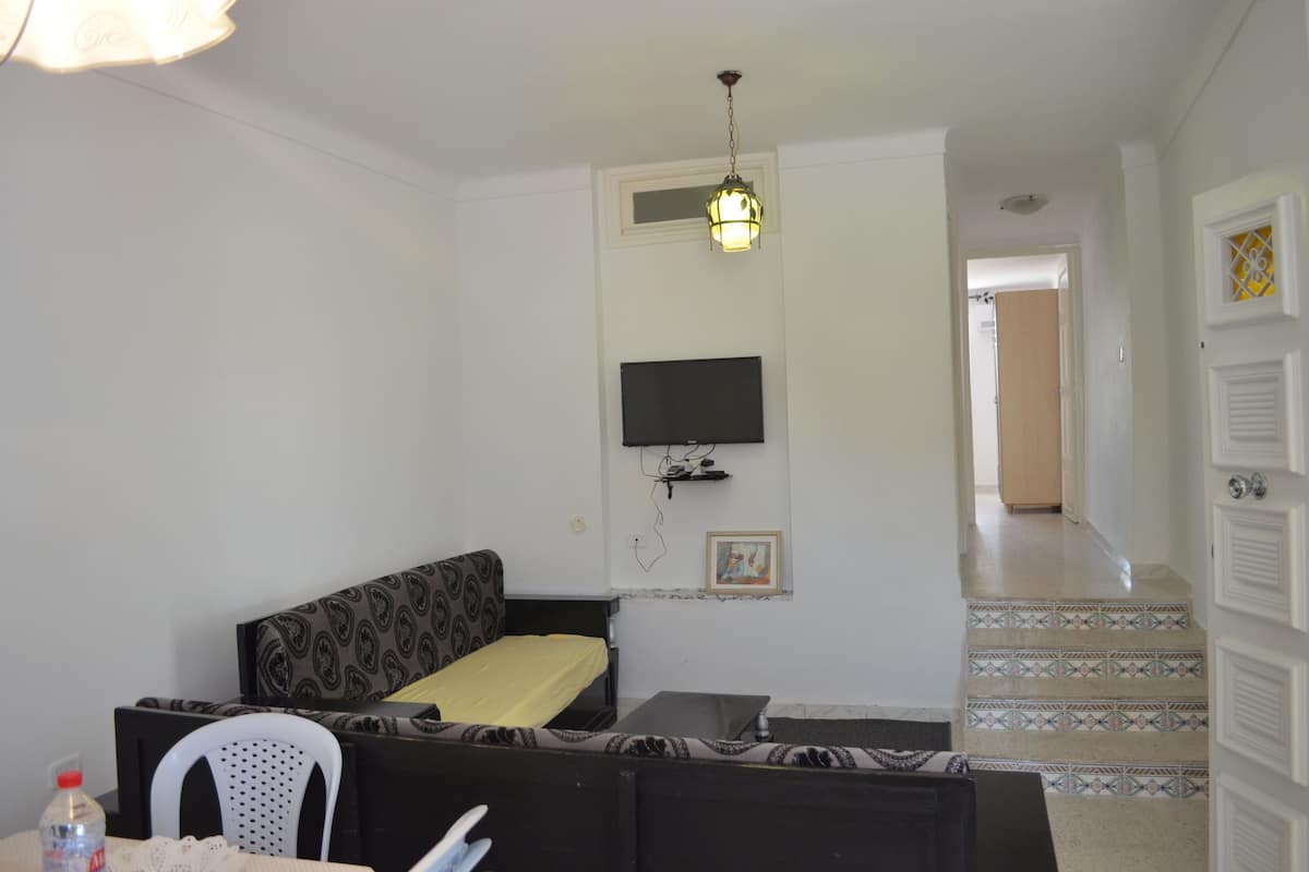 A small, simple room with a bed, a TV mounted on the wall, and a staircase leading to another area.
