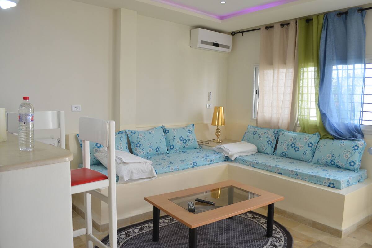 A living room with a sofa, a coffee table, a chair, and an air conditioning unit.