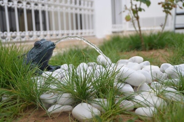 Un jardín con una estatua de rana, guijarros blancos y césped verde.