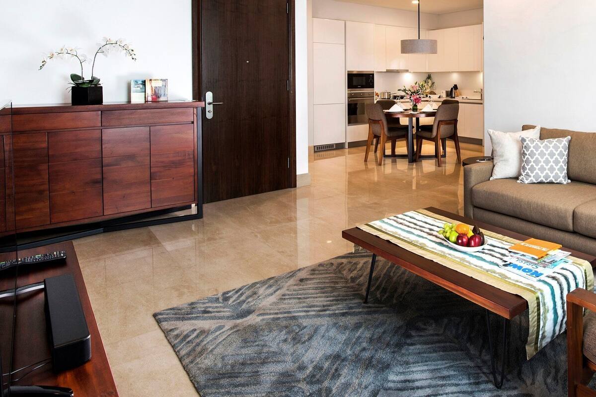 A living room with a sofa, armchairs, a coffee table with fruit, a TV, and a wooden cabinet.
