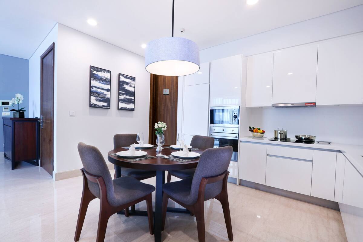 A modern kitchen with white cabinets, a dining table with chairs, and a pendant light.