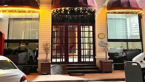 A hotel entrance with a sign reading 'Samson HOTEL KAPRIS,' large arched windows, and a decorative awning.
