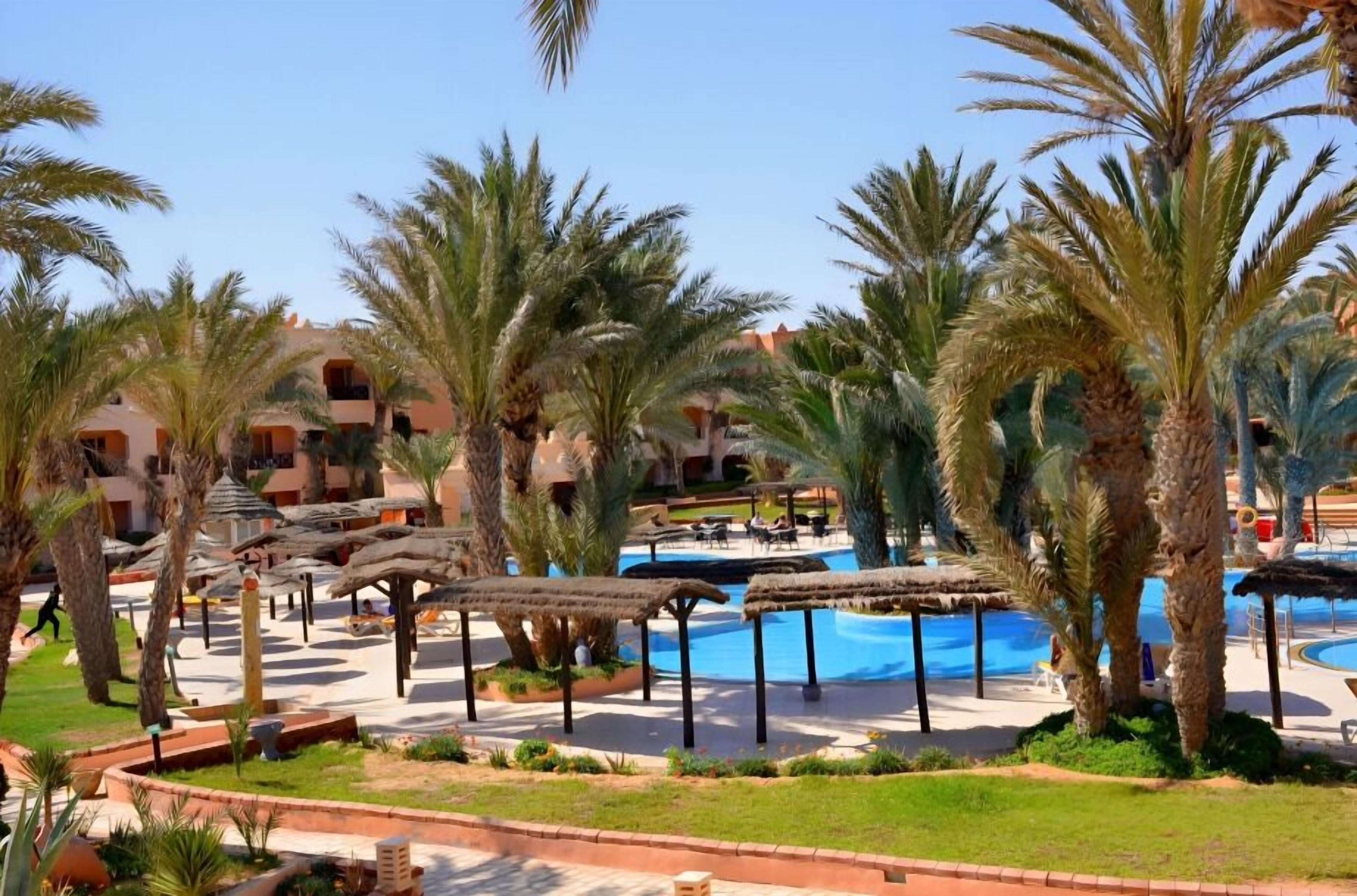 Un resort con piscina, palmeras y construcciones de techo de paja.