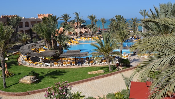 Un complexe hôtelier doté d’une piscine, de chaises longues, de palmiers et offrant une vue sur la mer.