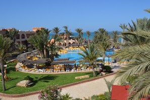 Ett semesterparadis med en swimmingpool, solstolar, palmer och utsikt över havet.