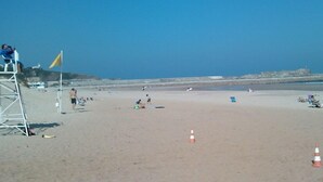 A beach with lifeguard chairs, a flag, and beachgoers. - Casas Rurales El Terrero (Valdaliga)