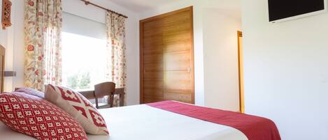 A bedroom with a bed, curtains, a wooden door, a TV, and a chair.