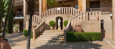 Un edificio de ladrillo con una escalera central, palmeras y una estatua en la parte superior.