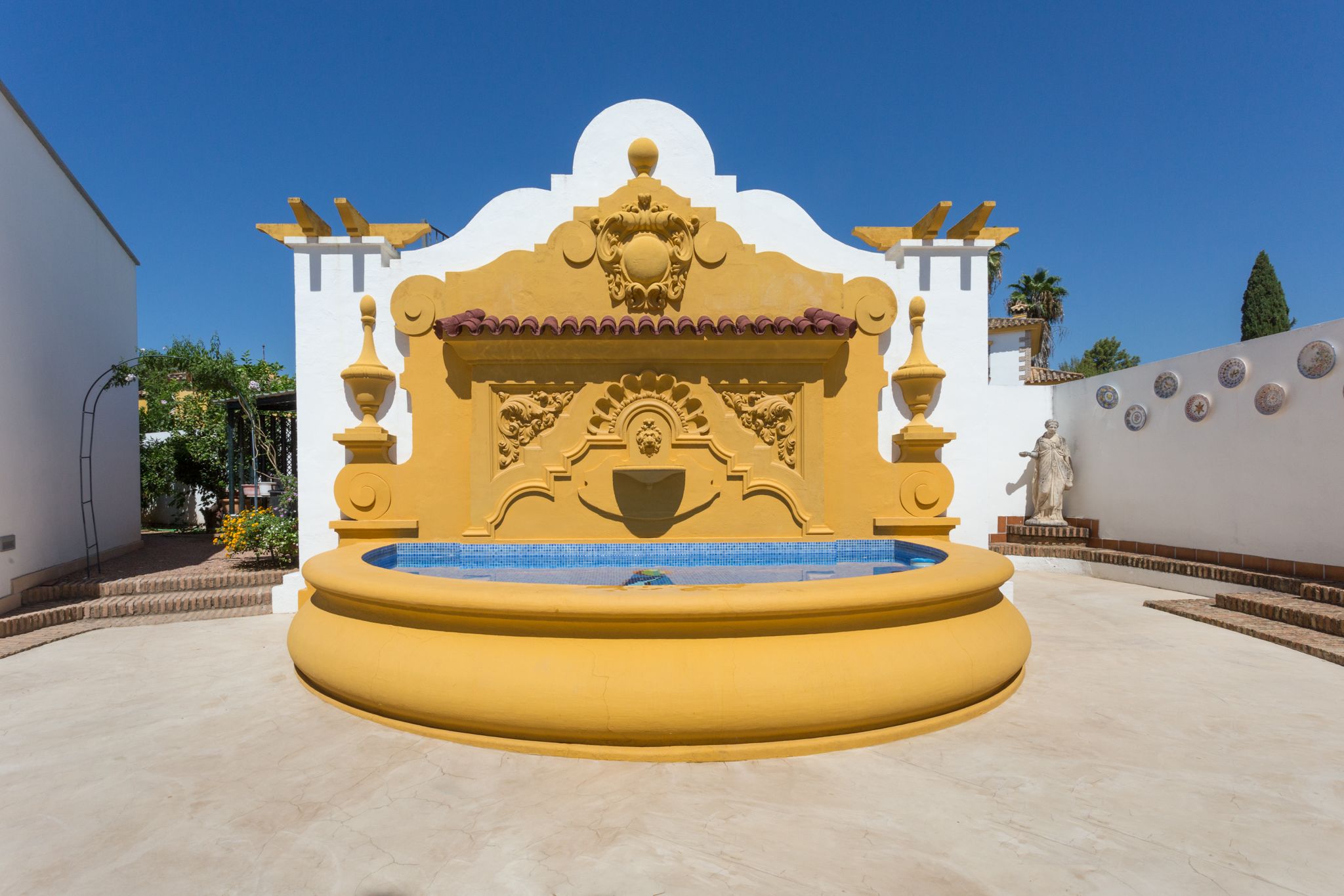 A fountain with a yellow base and a decorative white wall behind it.
