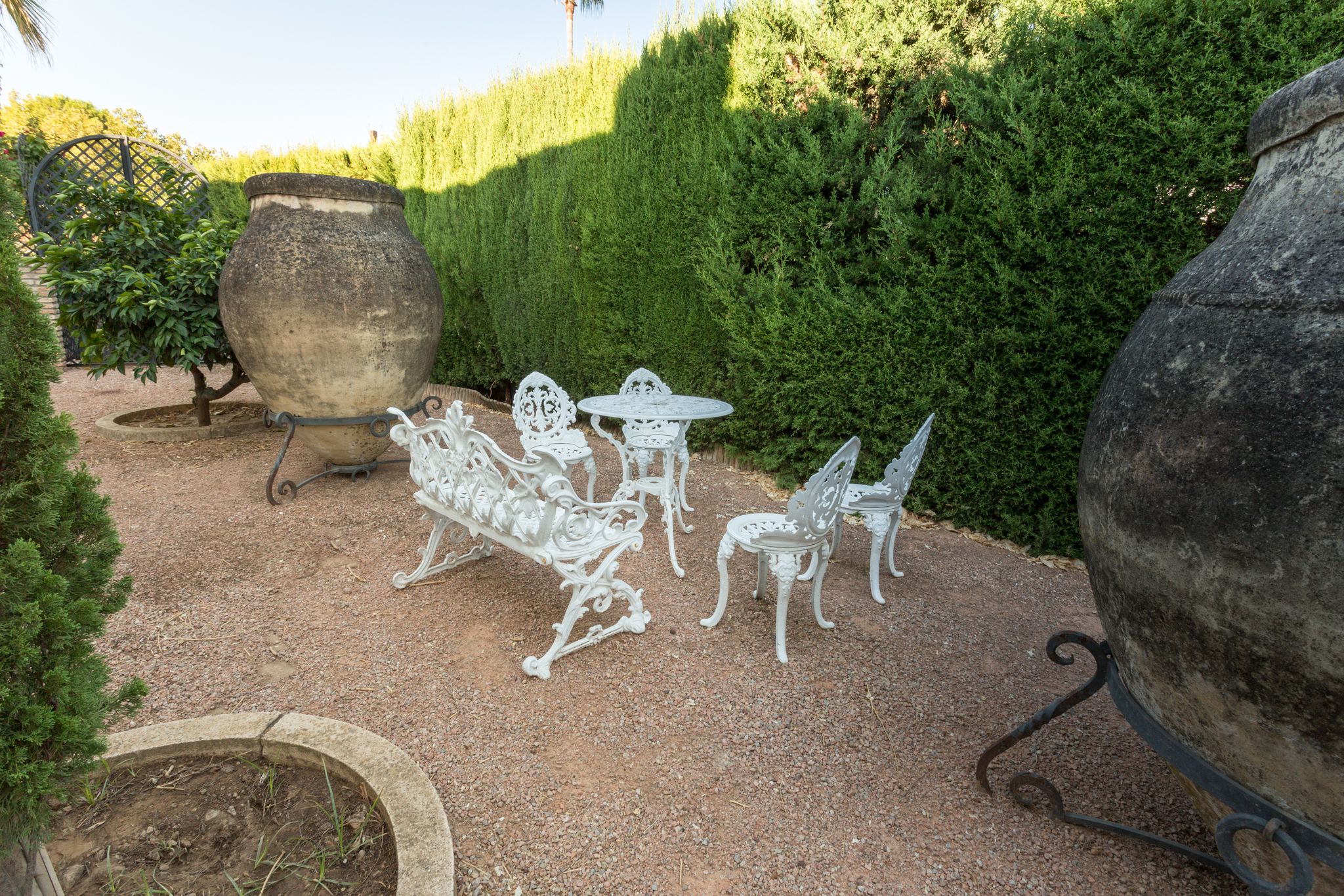 A garden patio with white metal furniture, including a bench, chairs, and a table.
