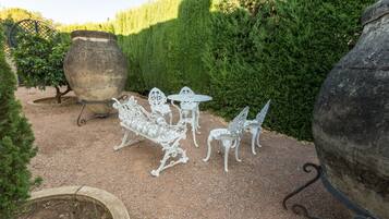 A garden patio with white metal furniture, including a bench, chairs, and a table.
