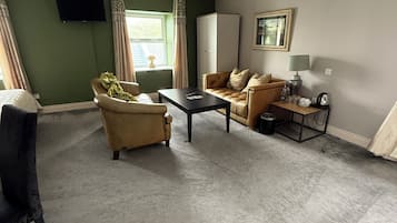 A living room with a sofa, armchair, and coffee table. There is a television on the wall and a window with curtains.