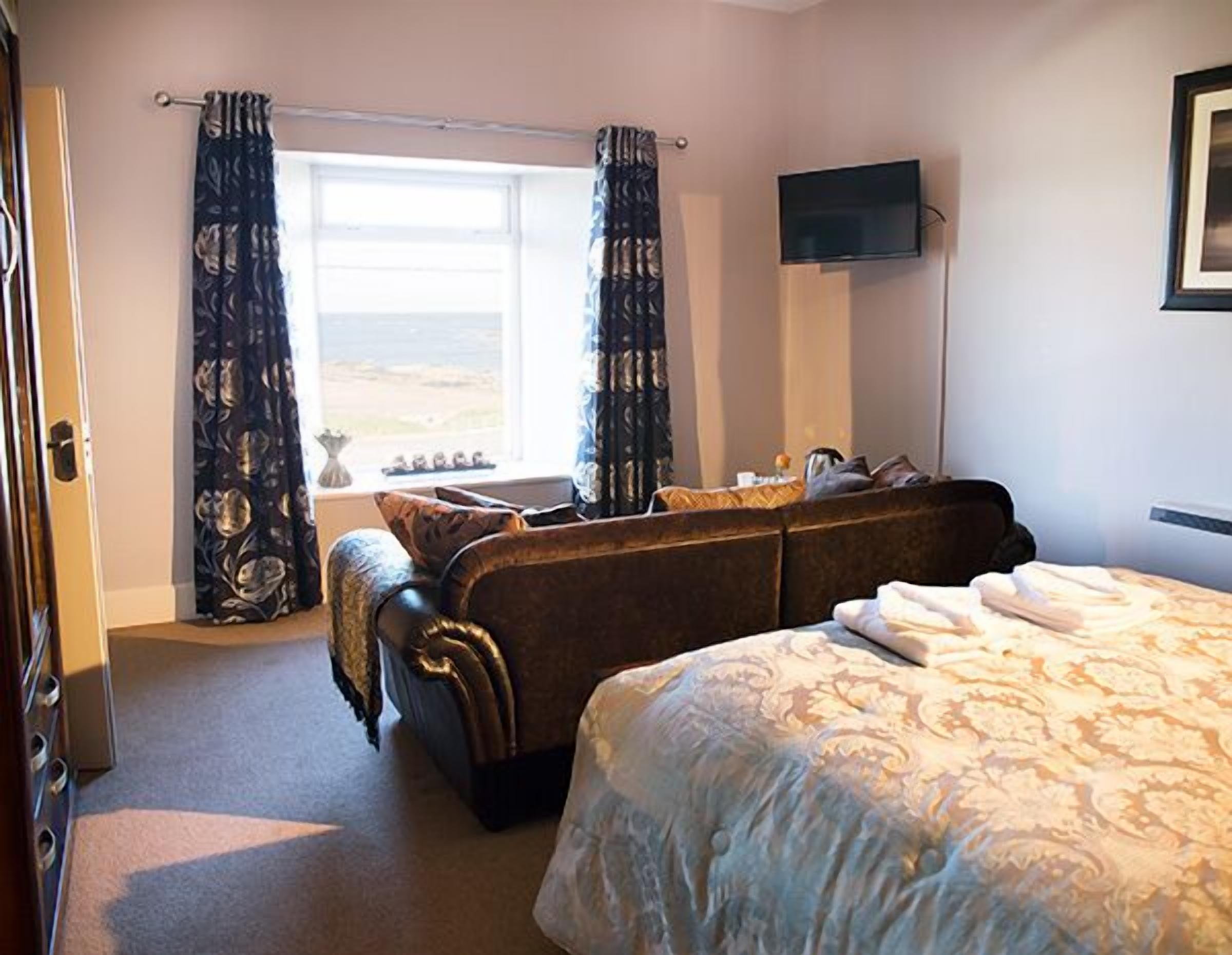 Une chambre d’hôtel avec un grand lit, un canapé, une télévision et une fenêtre avec des rideaux.