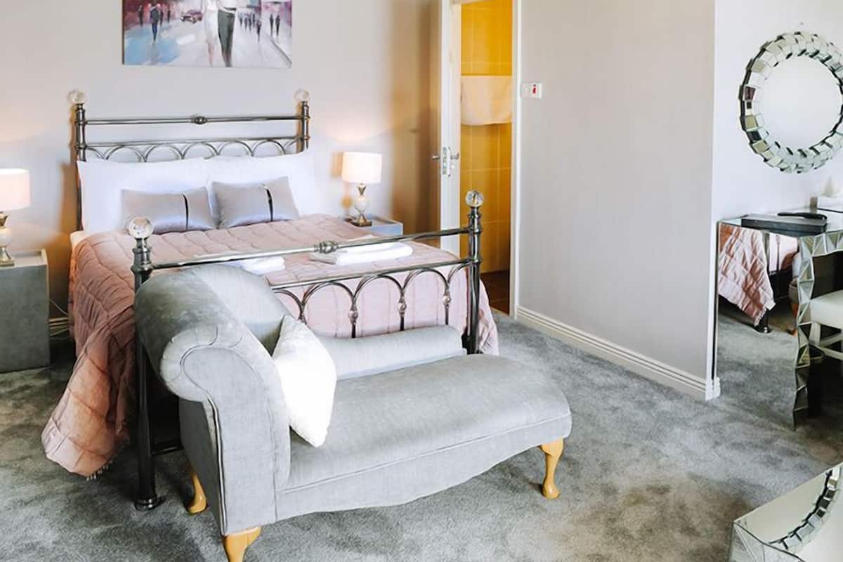 Une chambre à coucher avec un lit, des tables de chevet, une chaise, un miroir et un tableau accroché au mur.
