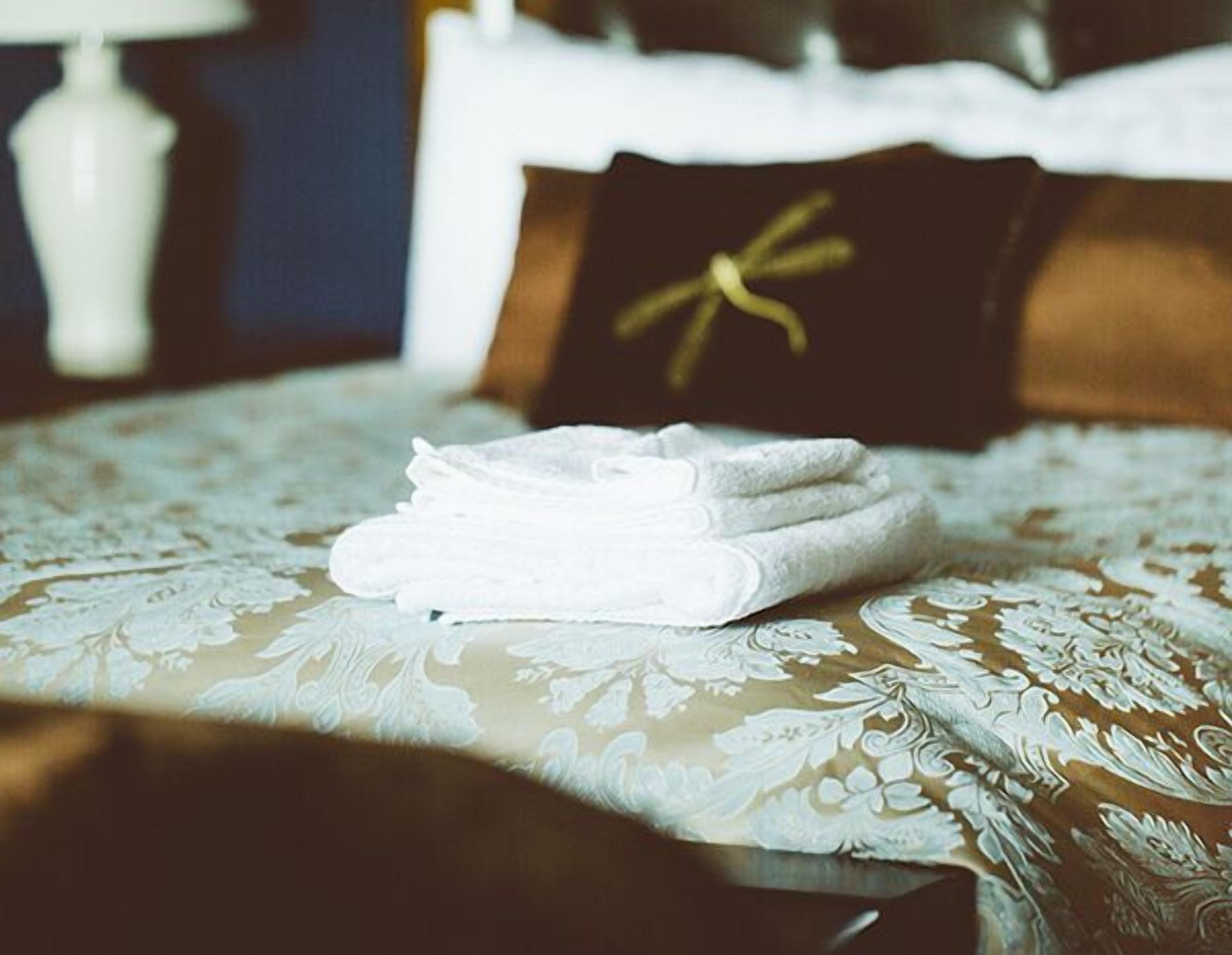 Un juego de toallas blancas ordenadamente dobladas sobre una cama con edredón estampado de flores.