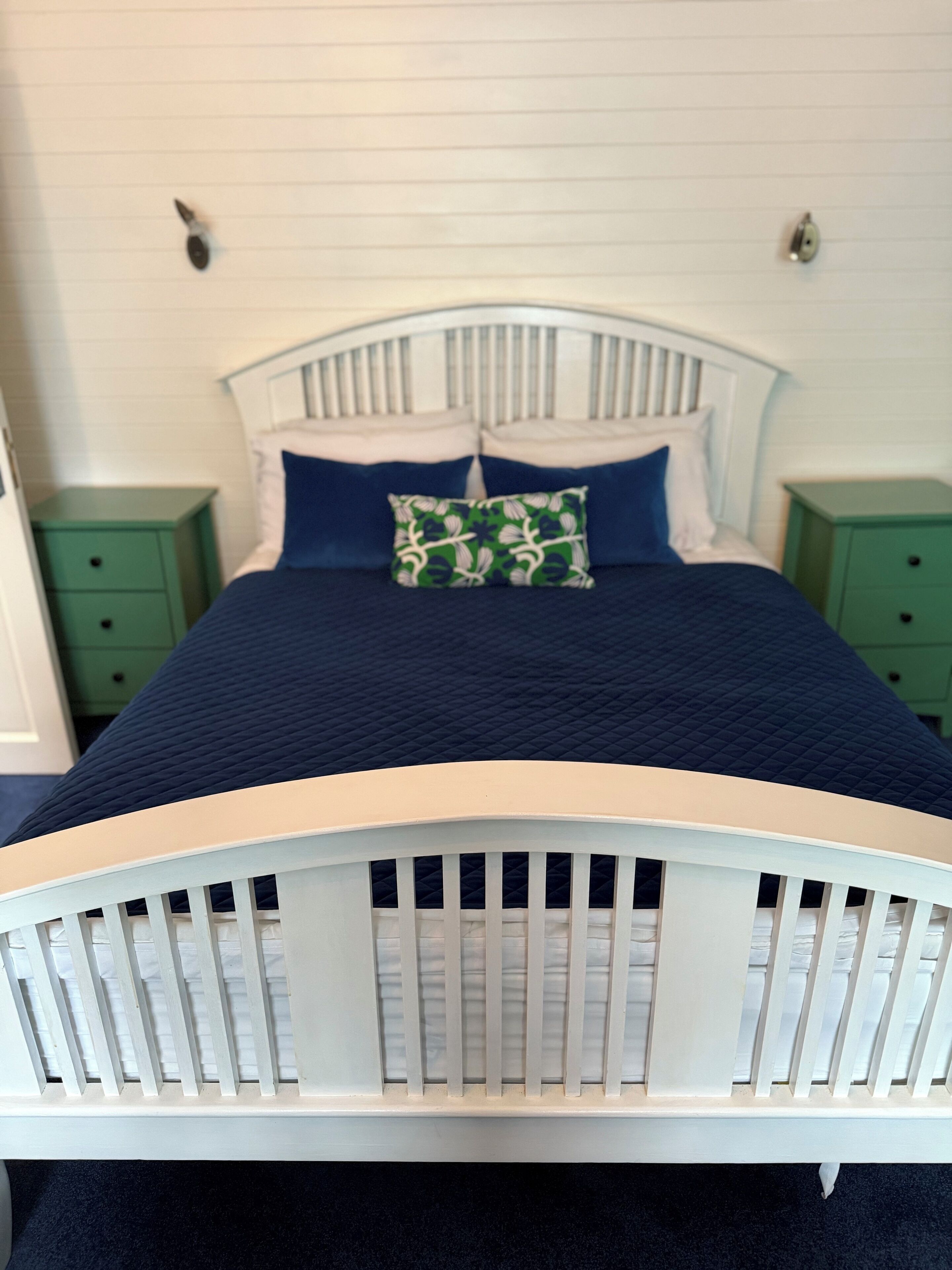 A bed with a white headboard, two green nightstands, and a blue bedspread with a green pillow.