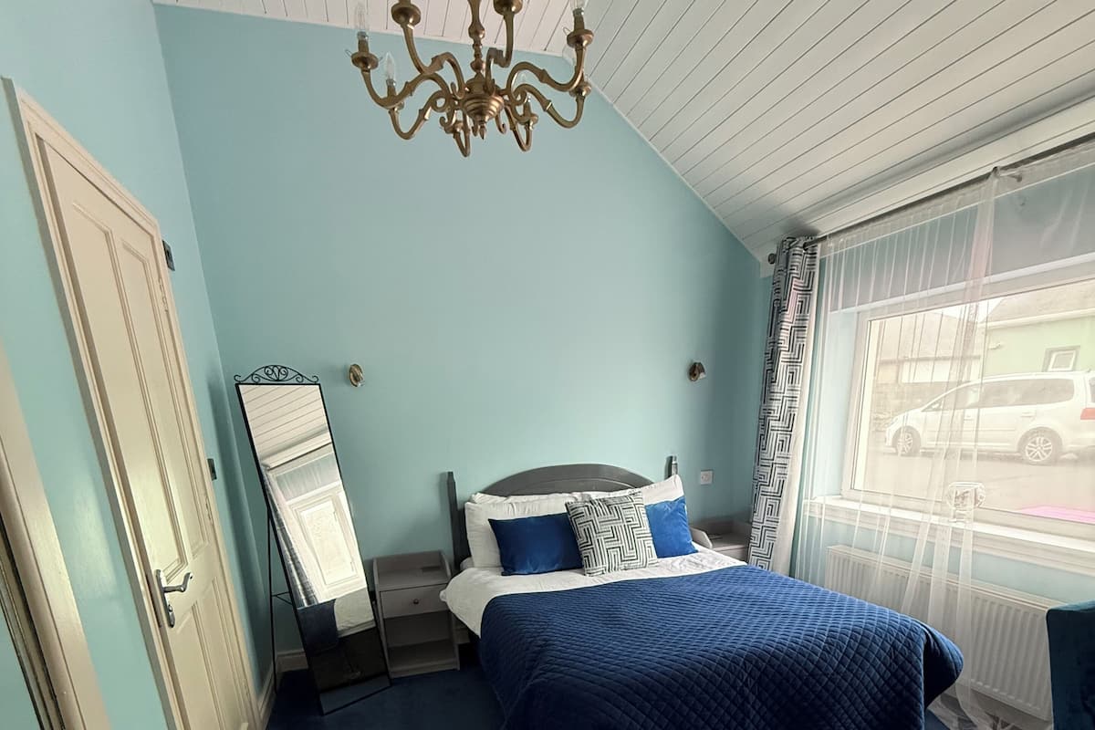 Une chambre à coucher avec un lit, un bureau, un miroir et une fenêtre donnant sur une voiture garée à l’extérieur.
