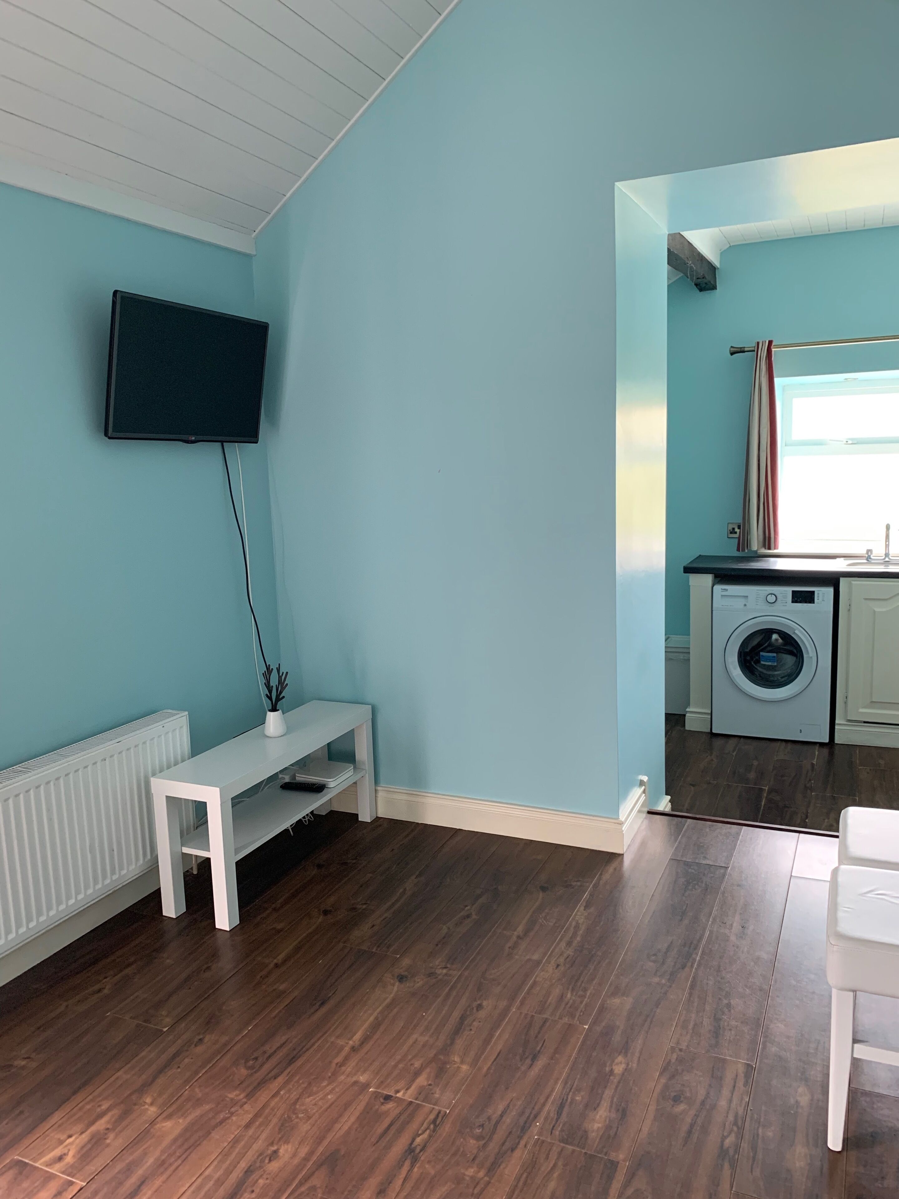 A room with a white bench, a TV mounted on the wall, a washing machine, and a radiator.