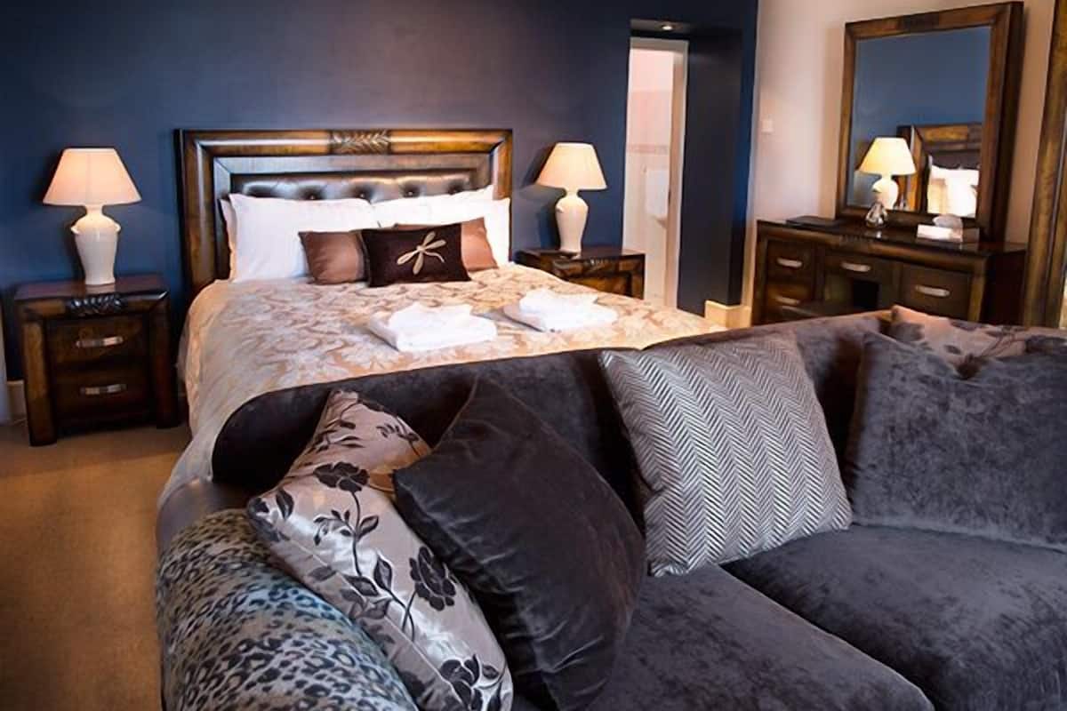 Une chambre d’hôtel avec un grand lit, deux tables de chevet avec des lampes, un canapé de couleur sombre et un miroir au mur.