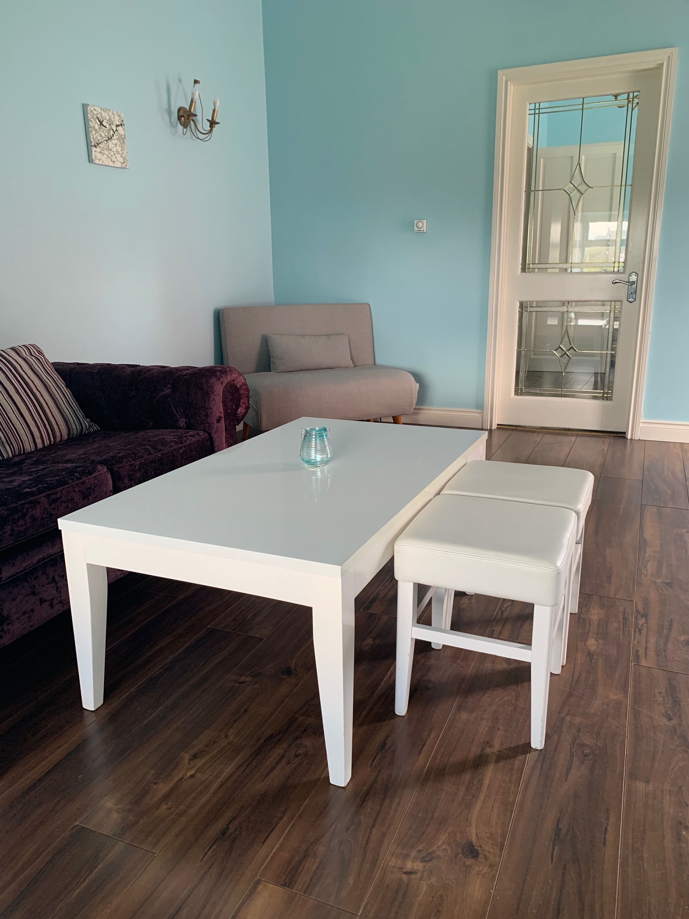 Una sala de estar con una mesa de centro blanca, un sofá color beige y una puerta de cristal con un diseño decorativo.
