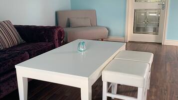 Una sala de estar con una mesa de centro blanca, un sofá color beige y una puerta de cristal con un diseño decorativo.