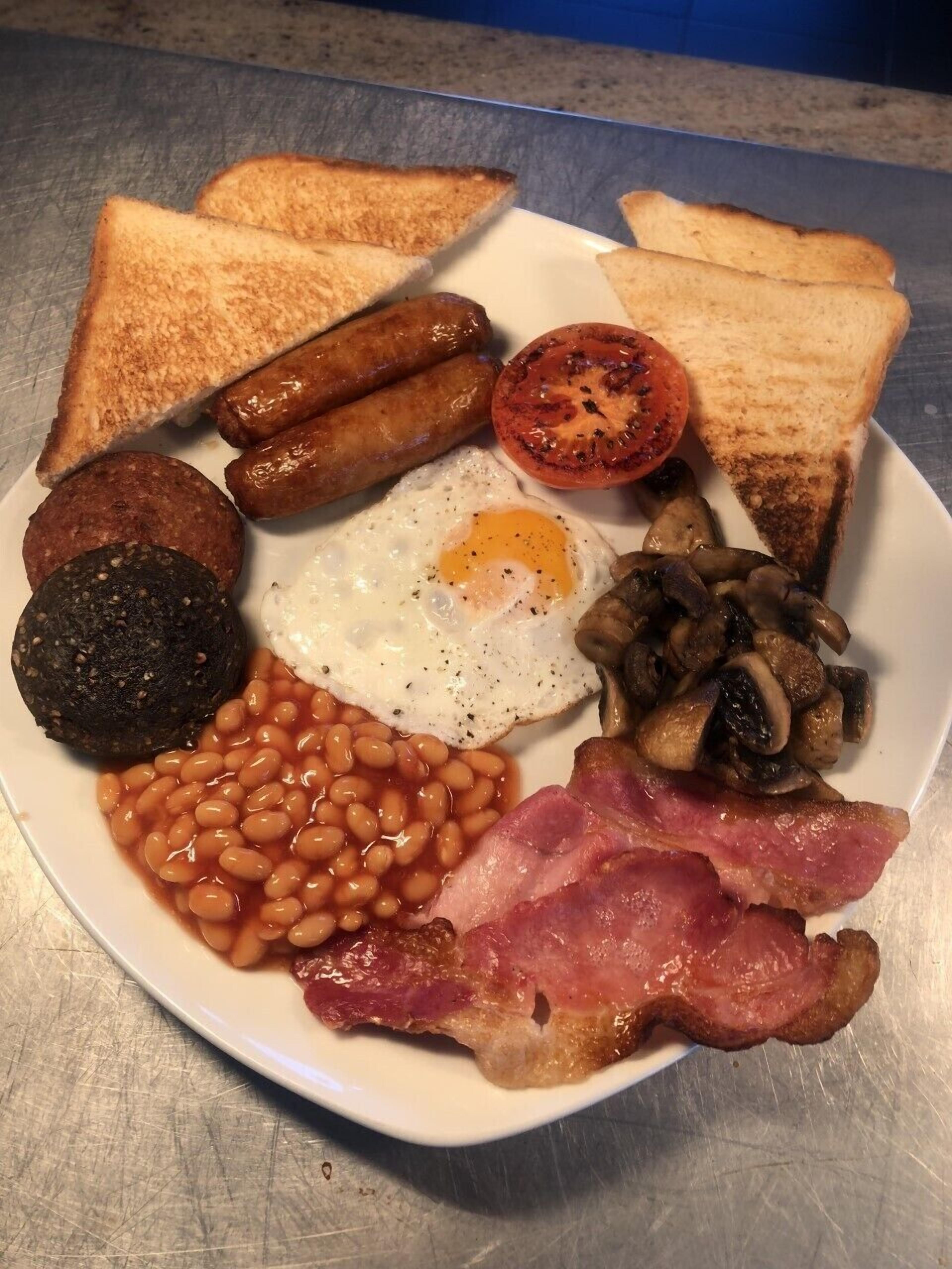 Un plato de comida para el desayuno con tostadas, salchichas, huevos, champiñones, frijoles y tocino.