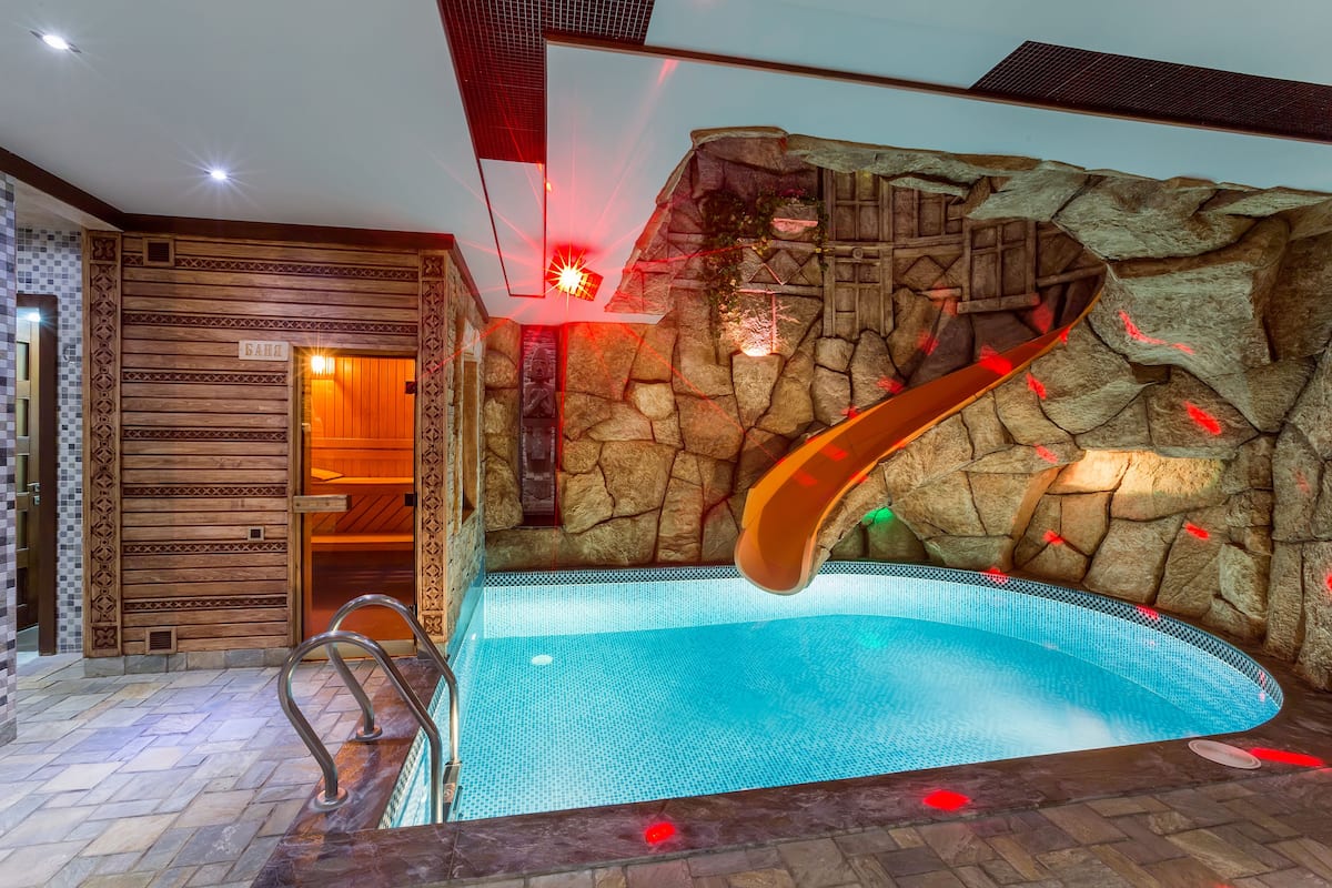 Una piscina con tobogán, pared de madera y suelo de baldosas.