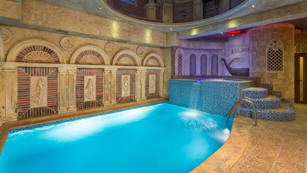 Una piscina interna con pavimento in pietra e una parete decorata con archi e statue.