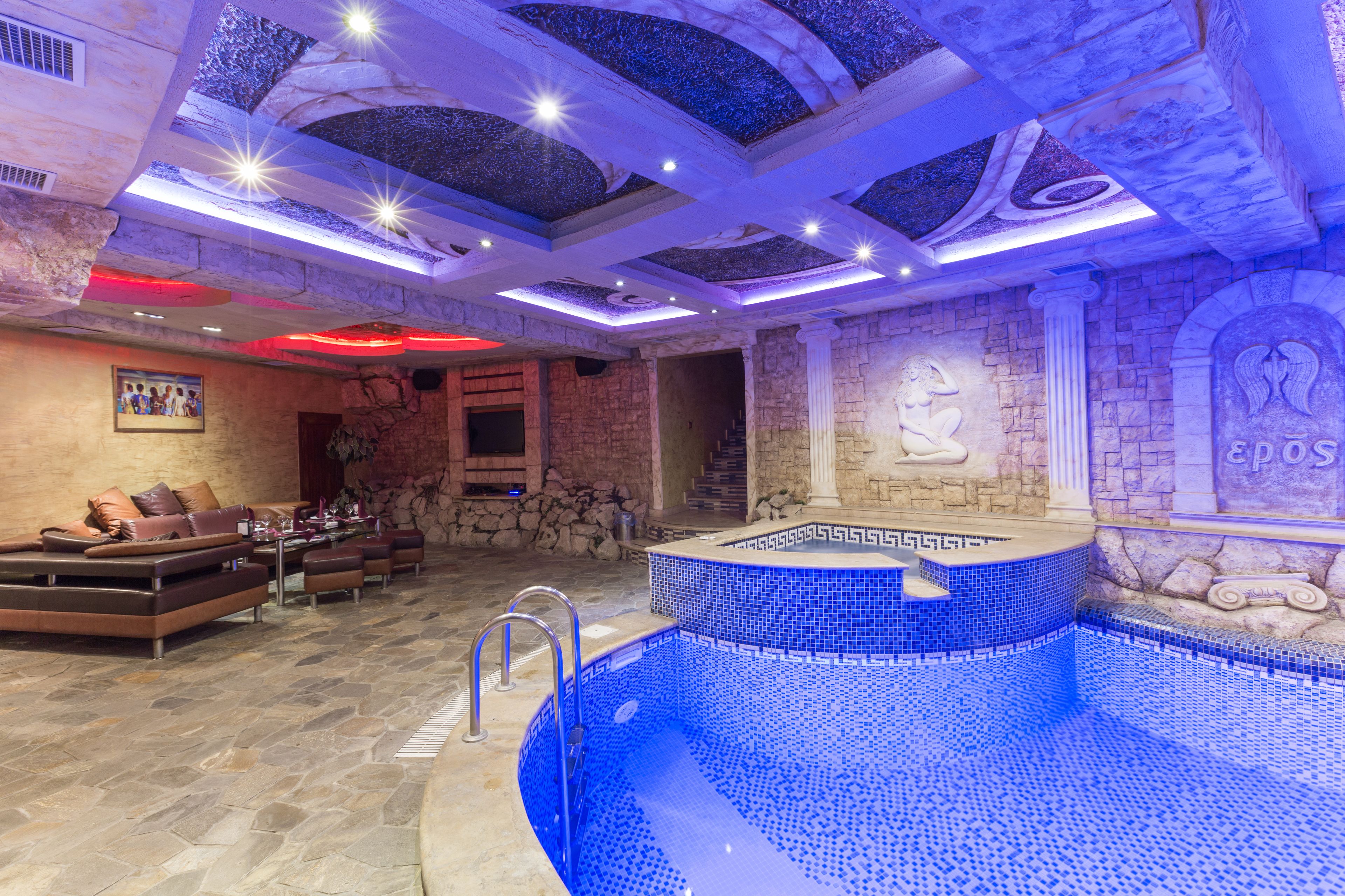 Ein luxuriöser Innenpoolbereich mit Steinwänden, einem blau gefliesten Pool und moderner Beleuchtung.