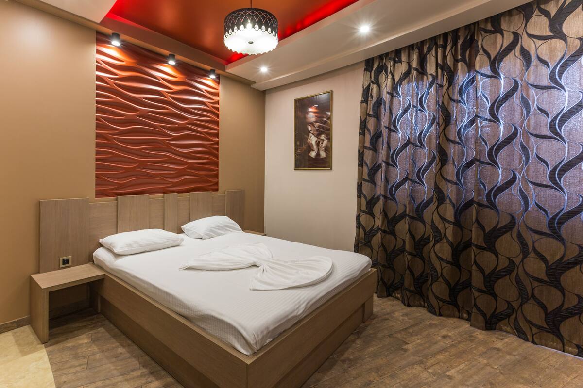 Una habitación de hotel moderna con una cama de madera, una mesita de noche, una cortina estampada y un diseño de pared original.