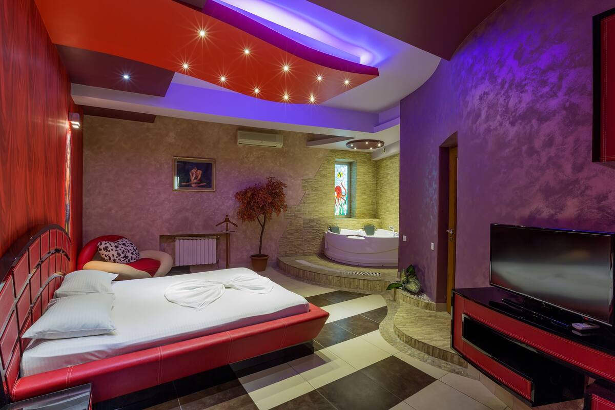 Un dormitorio moderno con una cama grande, un televisor, una bañera y un baño pequeño.