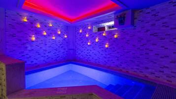 Un moderno spa con piscina de azulejos azules, bancos de madera e iluminación ambiental.