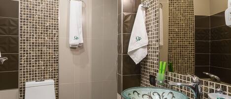 A modern bathroom with a glass sink, a toilet, and a shower area.