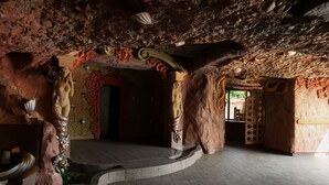 Una habitació amb sostre de pedra, sòl de fusta corbat i una porta amb un arc decoratiu.