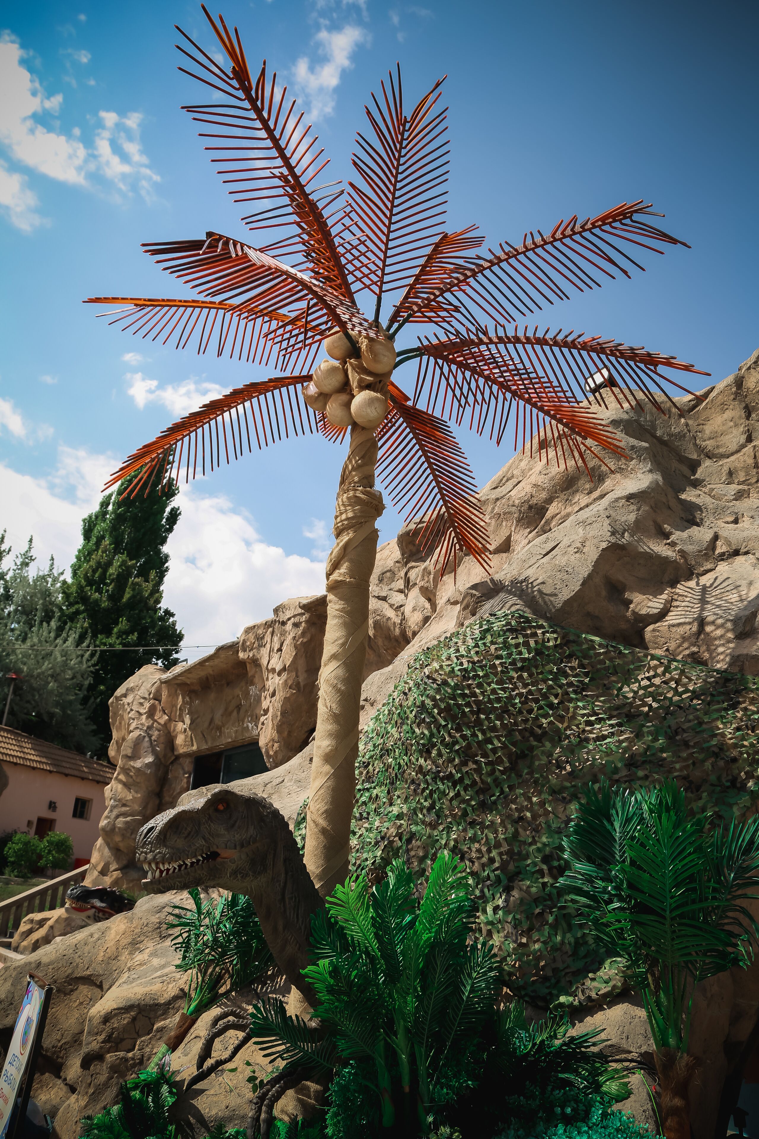 Um modelo de dinossauro com uma palmeira em frente a um fundo rochoso.