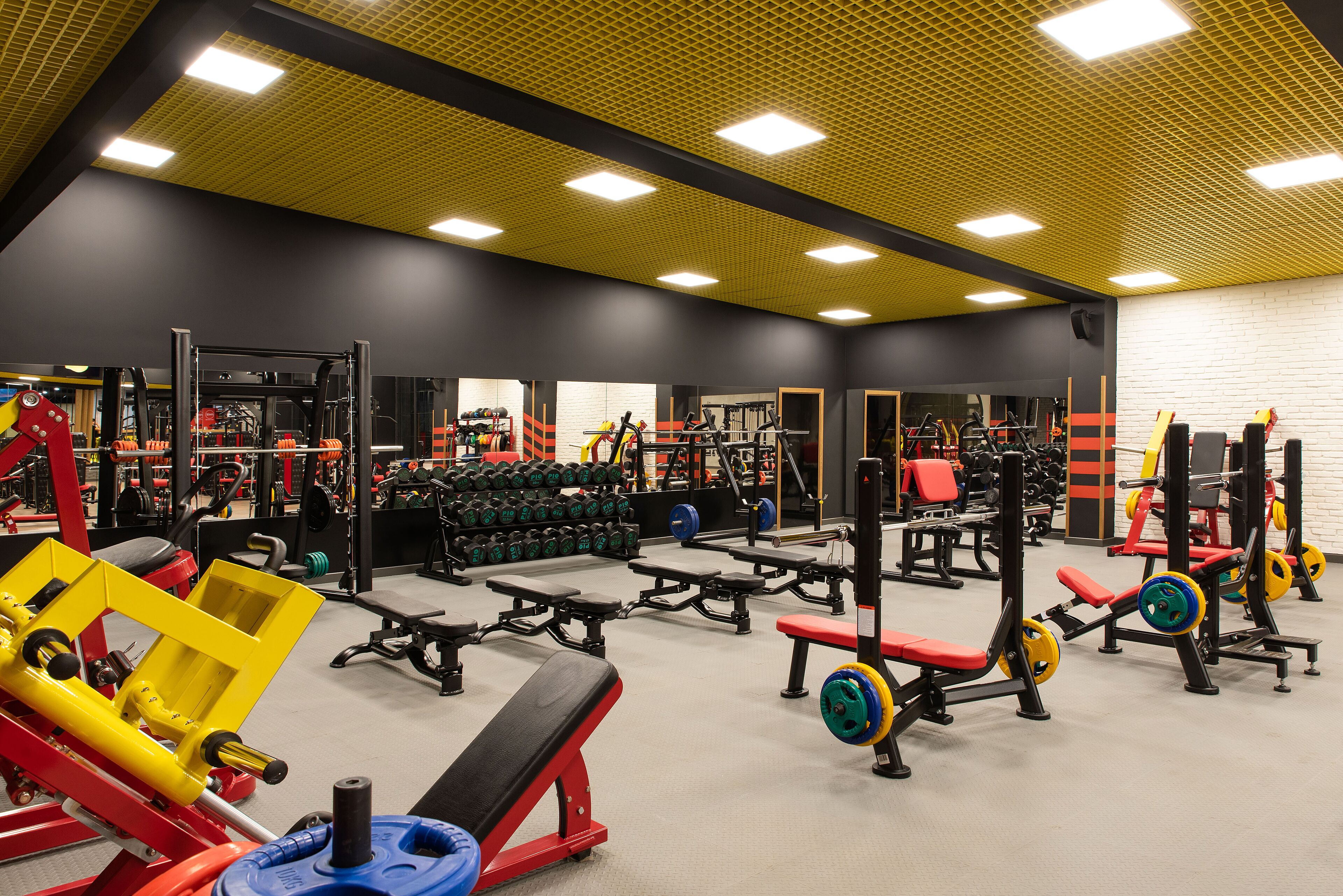 A gym with various weightlifting equipment, benches, and dumbbells.