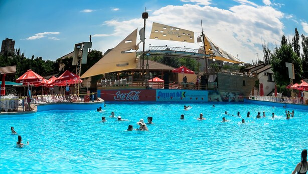 Una piscina amb gent nedant i prenent el sol, envoltada d'ombrel·les i un cartell de Coca-Cola.