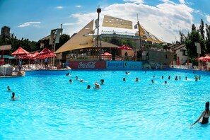 A swimming pool with people swimming and sunbathing, surrounded by umbrellas and a Coca-Cola sign. - Aquapark Hotel & Villas (Yerevan)