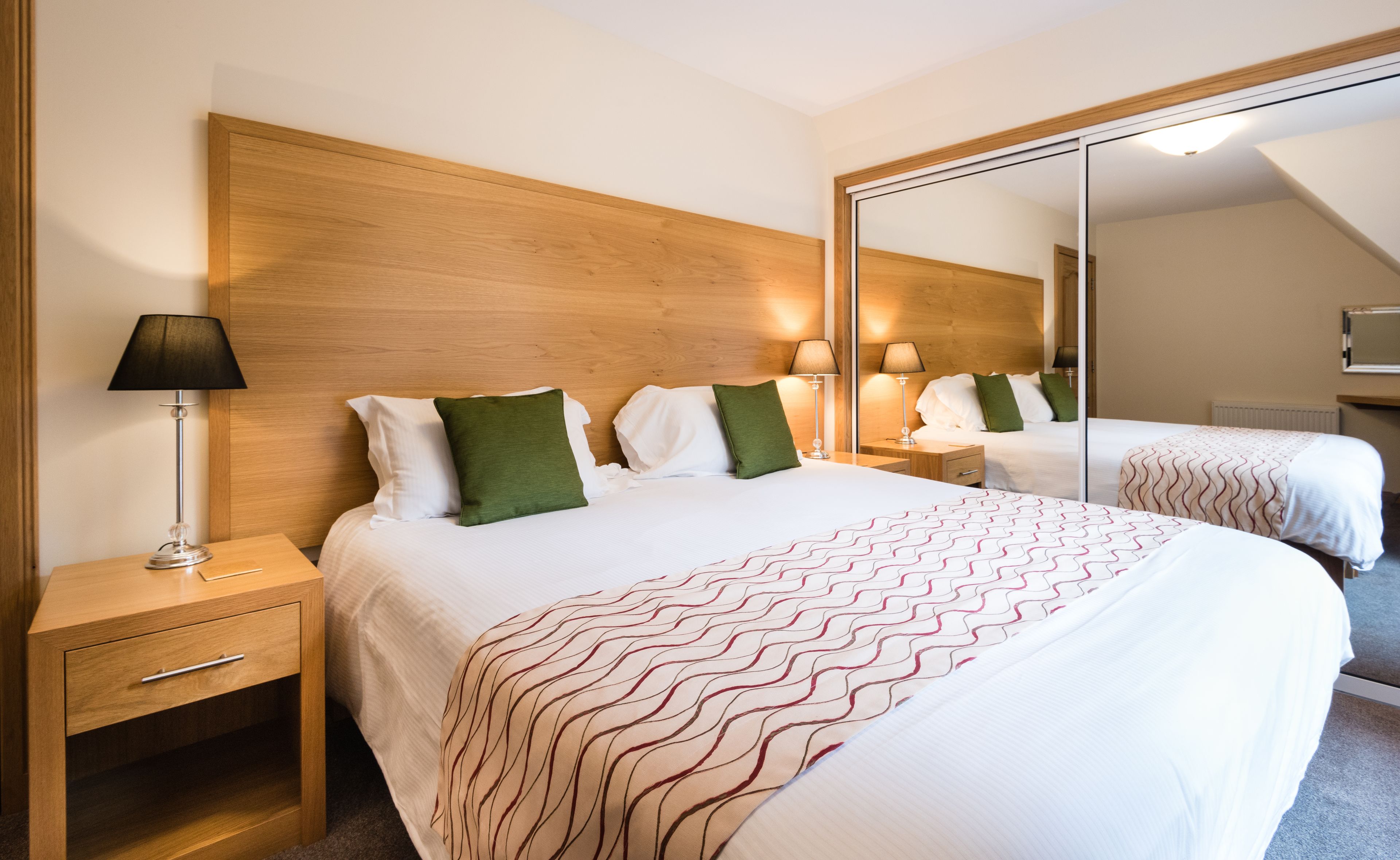 Ein Hotelzimmer mit einem großen Bett, einem Nachttisch, einem Spiegel und einer Lampe.