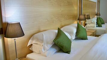 Un lit bien fait, avec du linge de lit blanc et des coussins verts, une lampe de chevet et une tête de lit en bois.
