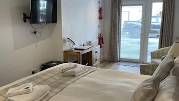 Habitación de hotel con una cama grande, un escritorio, un televisor de pantalla plana montado en la pared, un extintor y vistas al exterior a través de una puerta corredera.