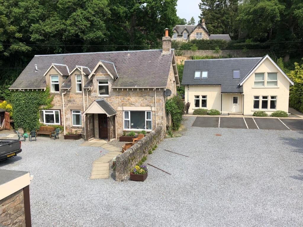 A two-story stone house with a driveway and a parking area.