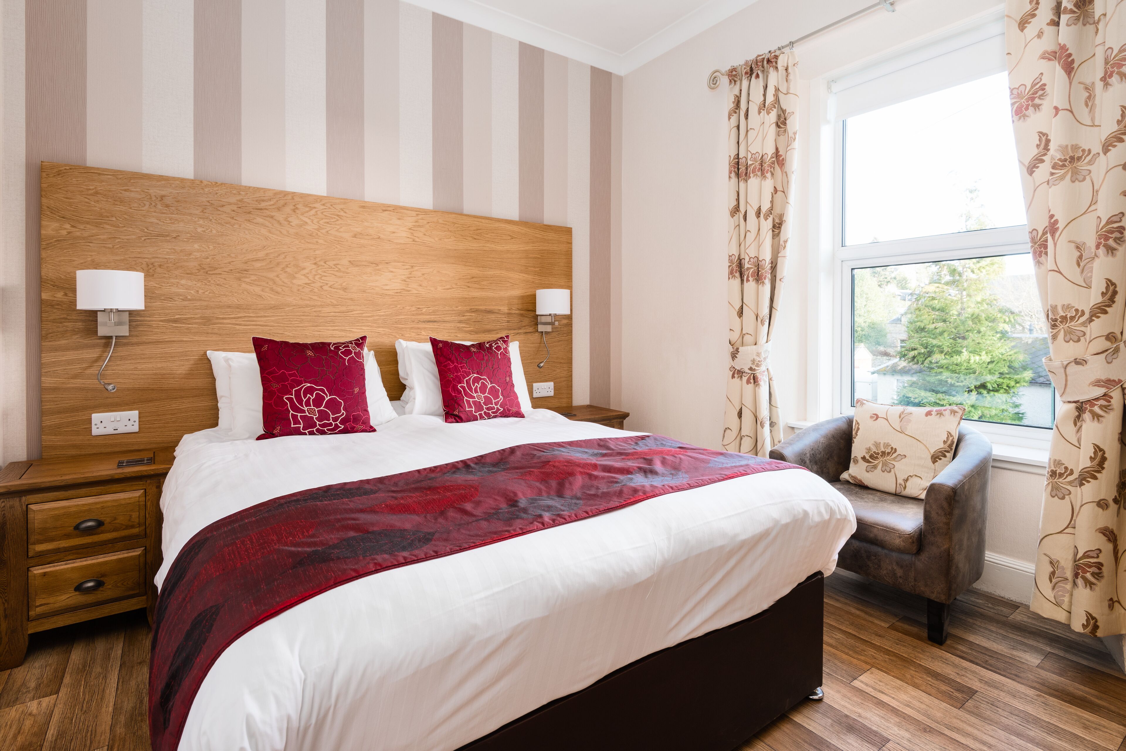 A neatly made bed with a red and white bedspread, a wooden headboard, and two bedside lamps.