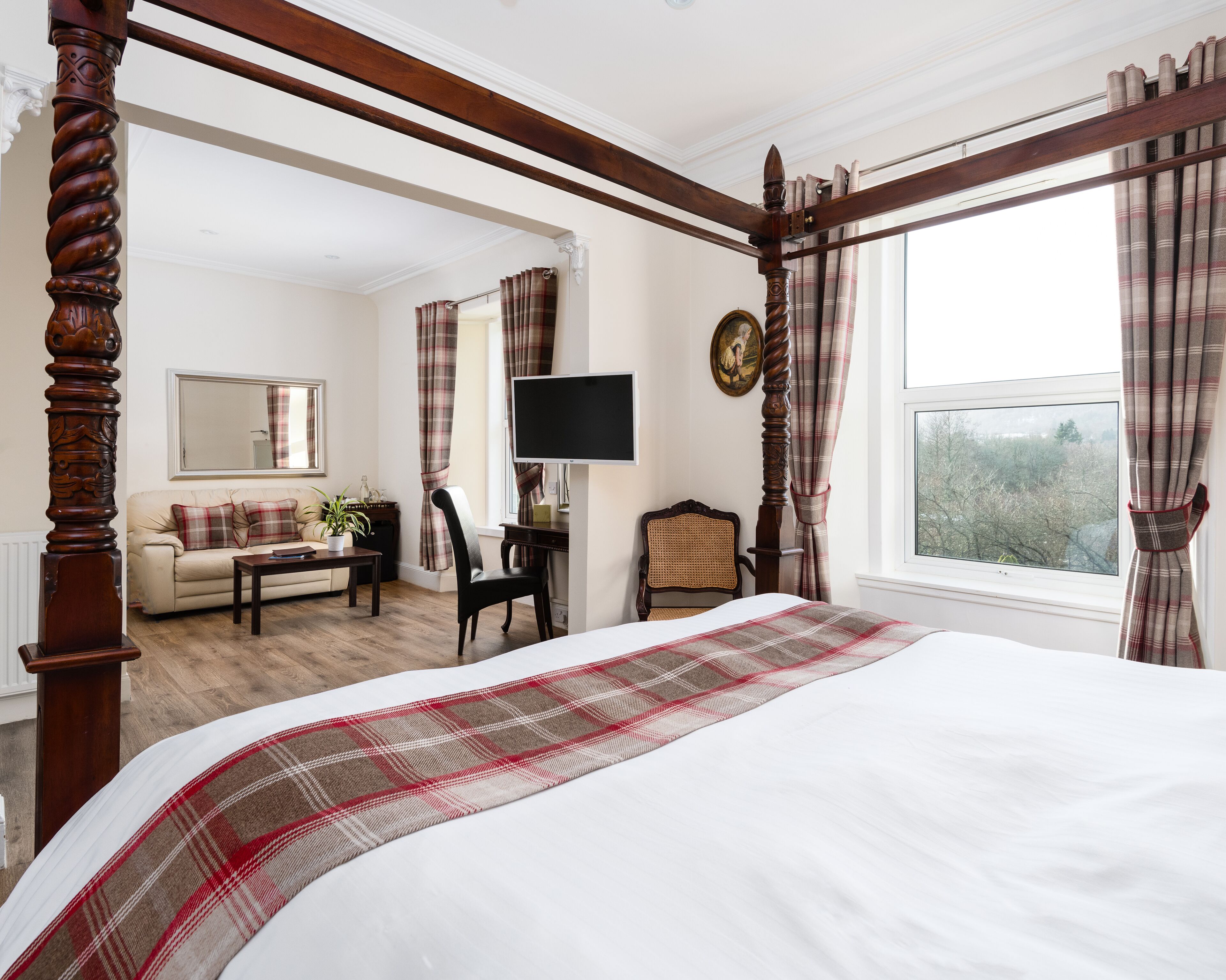 A bedroom with a four-poster bed, a television, a sofa, and a chair.