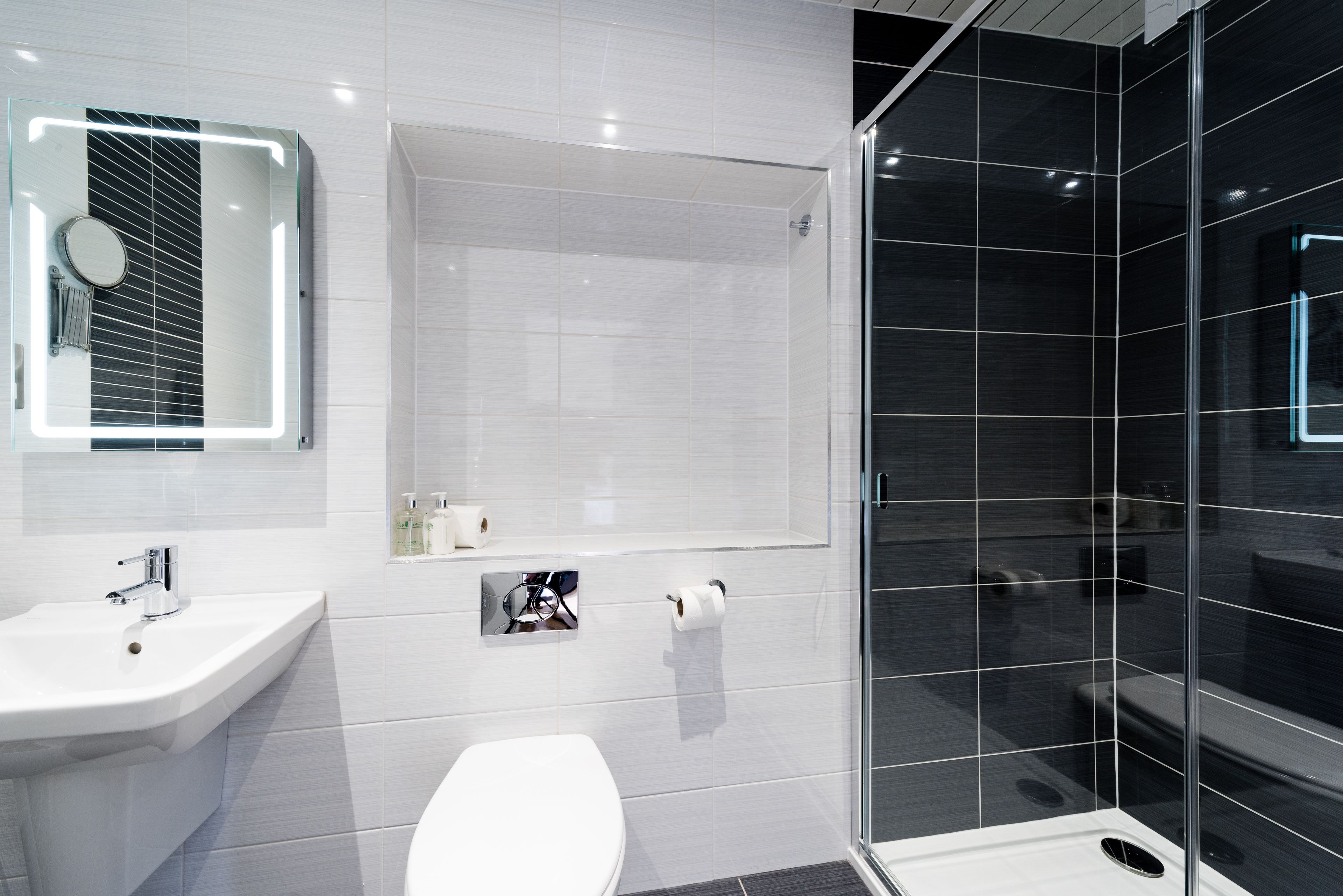 A modern bathroom with a glass shower enclosure, a white sink, and a mirror with built-in lighting.