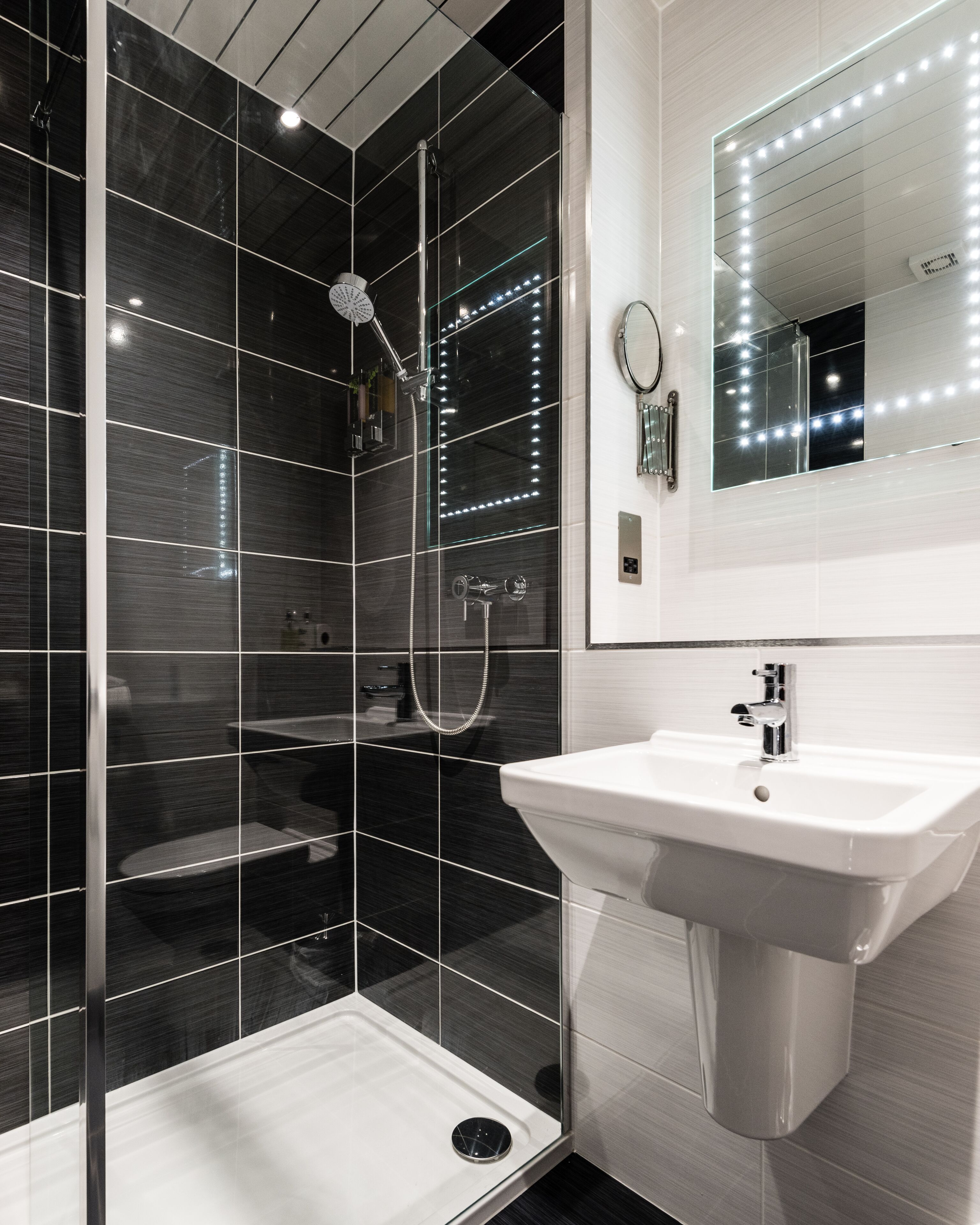 Une salle de bain moderne avec une douche à parois de verre, un lavabo blanc et un miroir avec éclairage intégré.
